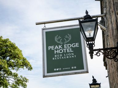 A sign for Peak Edge Hotel Red Lion Restaurant hanging from a metal bracket on a stone wall with a street lamp nearby