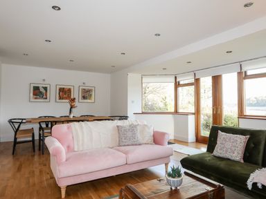 A living room with pink and green sofas a wooden dining table black chairs and large windows at Ynys Faelog Cottage in Ynys Faelog near Menai Bridge