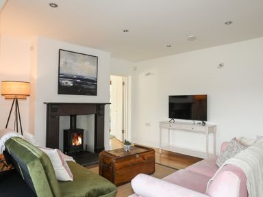 A living room with a green sofa pink sofa wooden trunk coffee table TV on white stand and fireplace at Ynys Faelog Cottage in Ynys Faelog near Menai Bridge