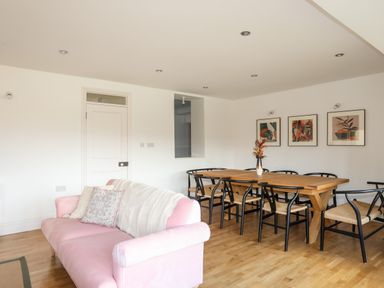 A living room with a pink sofa and a wooden dining table with black chairs at Ynys Faelog Cottage in Ynys Faelog near Menai Bridge