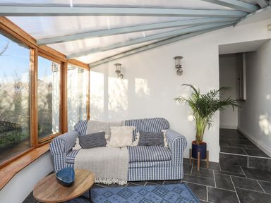 A sitting area with a blue plaid sofa and cushions beside large windows and a potted plant on a tiled floor at Ynys Faelog Cottage Ynys Faelog near Menai Bridge