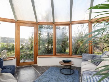 A sunroom with glass windows and door wooden frames sofas a round coffee table and a blue rug at Ynys Faelog Cottage in Ynys Faelog near Menai Bridge