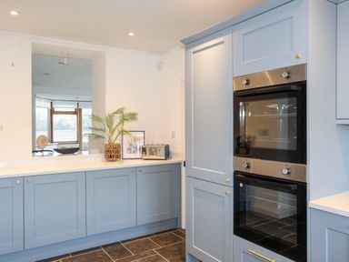 A kitchen with light blue cabinets double built in ovens a toaster plant and window overlooking another room at Ynys Faelog Cottage Ynys Faelog near Menai Bridge