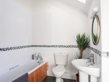 A bathroom with a bathtub wooden panel toilet sink round mirror and a tall green plant at Ynys Faelog Cottage Ynys Faelog near Menai Bridge