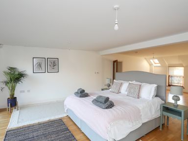 A bedroom with a bed with folded towels bedside tables a plant two framed pictures and two rugs on the floor at Ynys Faelog Cottage in Ynys Faelog near Menai Bridge