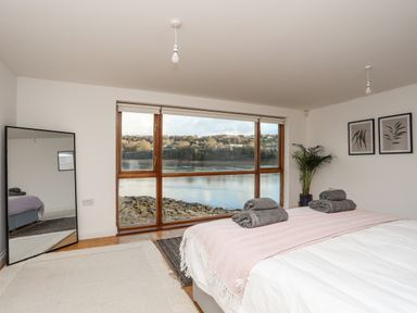 A bedroom with a bed towels on it a large floor mirror a plant and window overlooking water at Ynys Faelog Cottage Ynys Faelog near Menai Bridge