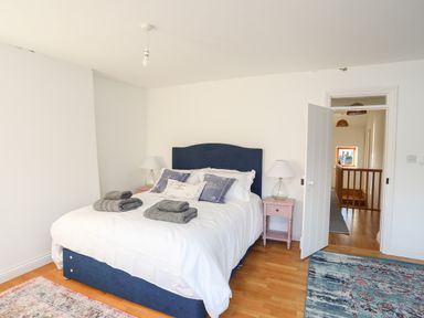 A bedroom with a blue bed headboard white bedding and folded towels on the bed flanked by pink bedside tables with lamps at Ynys Faelog Cottage in Ynys Faelog near Menai Bridge