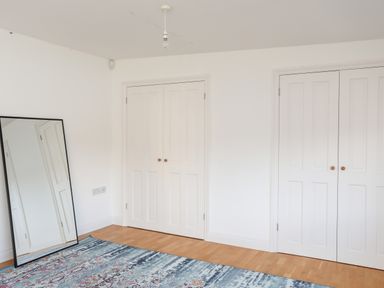 A room with two closed white closets a standing mirror and a patterned rug on a wooden floor at Ynys Faelog Cottage in Ynys Faelog near Menai Bridge