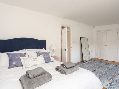 A bedroom with a bed with blue and white pillows folded towels a floor mirror a rug and closet doors at Ynys Faelog Cottage Ynys Faelog near Menai Bridge