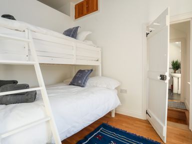 A bedroom with white bunk beds blue pillows and a blue rug at Ynys Faelog Cottage Ynys Faelog near Menai Bridge