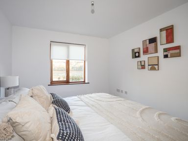 A bedroom with a bed and pillows near a window with a view of trees and water at Ynys Faelog Cottage Ynys Faelog near Menai Bridge