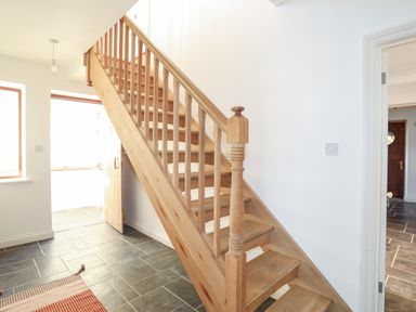 A wooden staircase in a hall with tiled floor and white walls at Ynys Faelog Cottage in Ynys Faelog near Menai Bridge