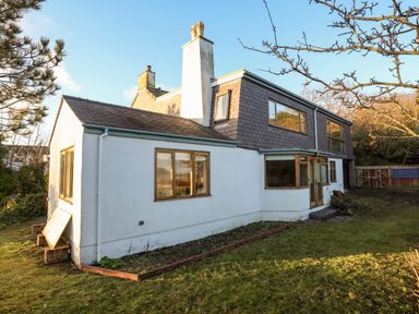 The exterior of a two story house with white walls and multiple windows and a grassy yard at Ynys Faelog Cottage in Ynys Faelog near Menai Bridge