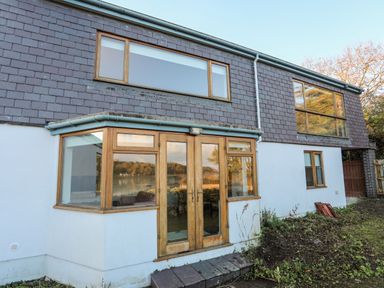 Exterior view of a two-story house with wooden framed windows and a glass door at Ynys Faelog Cottage in Ynys Faelog near Menai Bridge
