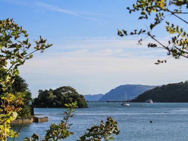 A view of a body of water with boats and islands framed by tree branches at Ynys Faelog Cottage Ynys Faelog near Menai Bridge