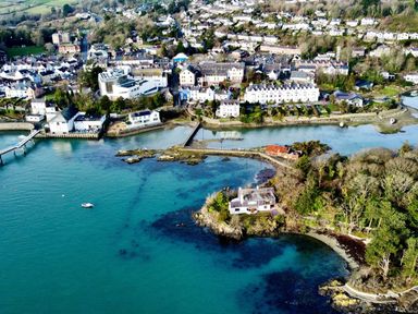 An aerial view of a coastal town with houses, trees, a pier, and a small boat in the water at Ynys Faelog near Menai Bridge