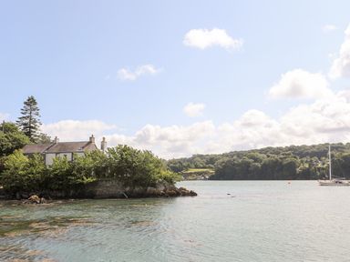 A house surrounded by trees near a body of water with a sailboat in the distance at Ynys Faelog near Menai Bridge