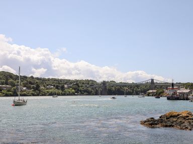 A river with boats and a suspension bridge in the background at Ynys Faelog near Menai Bridge