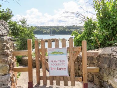 A wooden gate with a sign permitting access to Ynys Faelog with water and boats in the background at Ynys Faelog Cottage Ynys Faelog near Menai Bridge