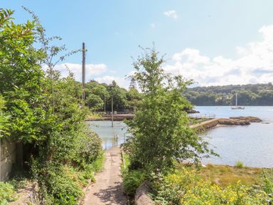 A pathway leading to a small pier with greenery on both sides and water with a boat in the background at Ynys Faelog Cottage Ynys Faelog near Menai Bridge