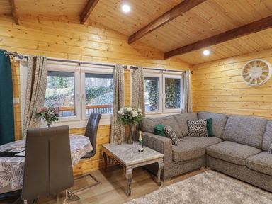 A living room with a gray sofa a coffee table with flowers and a bottle on it and a dining table with chairs at Buttermilk Bridge in Dungiven