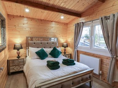 A bedroom with a bed with green pillows and towels bedside tables with lamps and a window with curtains at Buttermilk Bridge in Dungiven