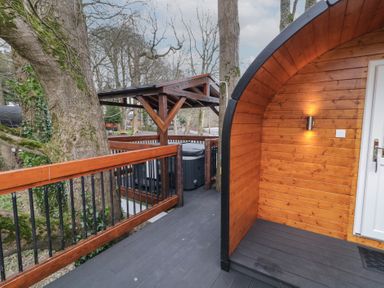 A wooden deck with railing surrounding a hot tub and the entrance to a wooden pod at Pine in Dungiven Londonderry