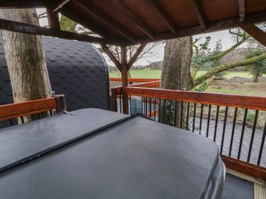 A covered wooden deck with a hot tub surrounded by trees and a view of a field at Pine in Dungiven Londonderry