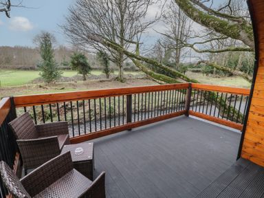 A wooden deck with two wicker chairs and a small table overlooking a stream and trees at Pine in Dungiven Londonderry