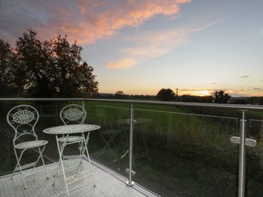 A balcony with a metal table and two chairs overlooking a field at sunset at Upper Annex in Quemerford