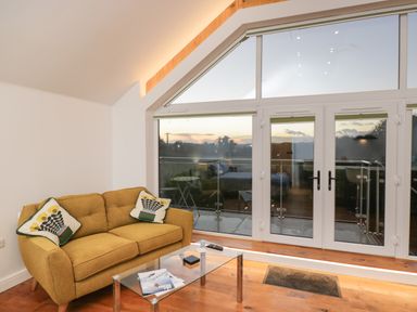 A small living room with a yellow sofa glass coffee table and large glass doors leading to a balcony at Upper Annex in Quemerford