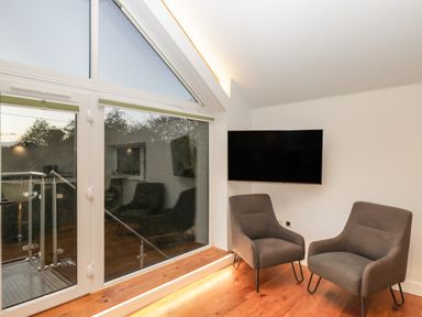 A room with two gray chairs a wall-mounted TV and large windows leading to a balcony at Upper Annex Quemerford