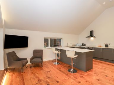 A kitchen with an island, bar stools, two chairs and a wall-mounted TV at Upper Annex in Quemerford
