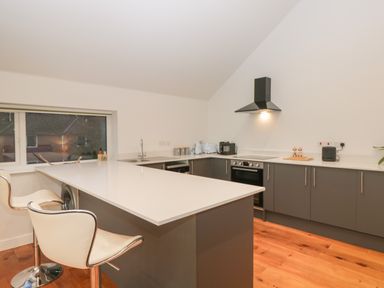 A kitchen with gray cabinets white countertops a built in oven and two white chairs at Upper Annex in Quemerford