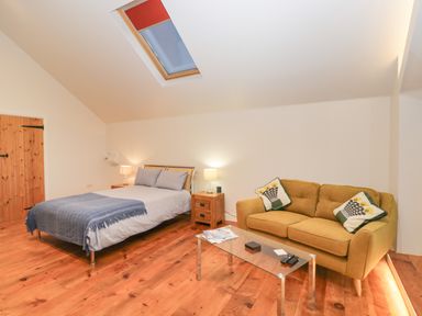 A bedroom with a double bed side tables lamps a skylight window a glass coffee table and a yellow sofa with cushions at Upper Annex in Quemerford