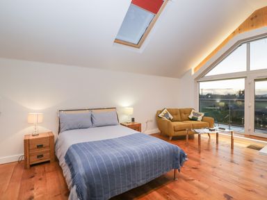 A bedroom with a bed blue bedspread two wooden nightstands with lamps a mustard sofa and glass doors at Upper Annex in Quemerford