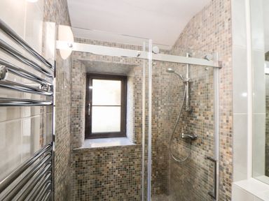 A bathroom with a tiled shower enclosure glass door and a window at The Old Piggeries in Gulval near Penzance