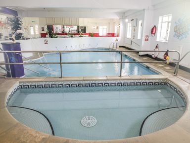 An indoor swimming pool area with a large pool and a smaller pool separated by a metal railing at The Old Piggeries in Gulval near Penzance