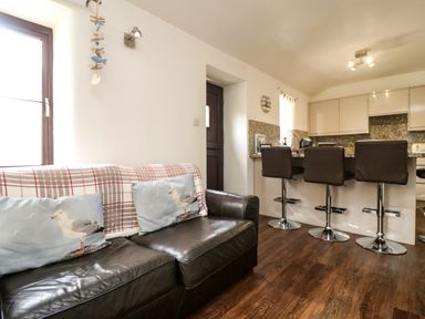A kitchen area with three bar stools and a leather sofa with seagull cushions at The Old Piggeries in Gulval near Penzance