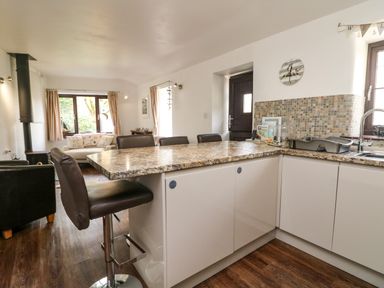 A kitchen and living area with bar stools a countertop and windows at The Old Piggeries in Gulval near Penzance