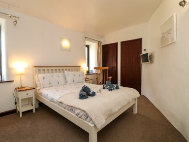 A bedroom with a double bed bedside tables a rocking chair and a wall-mounted TV at The Old Piggeries in Gulval near Penzance