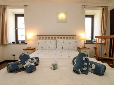 A bedroom with a double bed flanked by bedside tables and lamps rolled towels on the bed at The Old Piggeries in Gulval near Penzance