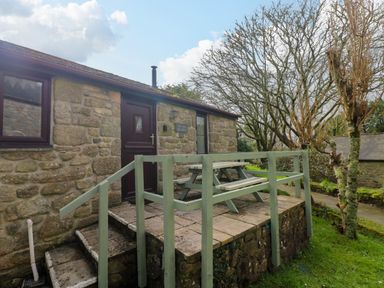 Stone cottage with a wooden picnic table on a small raised patio with green railings at The Old Piggeries in Gulval near Penzance