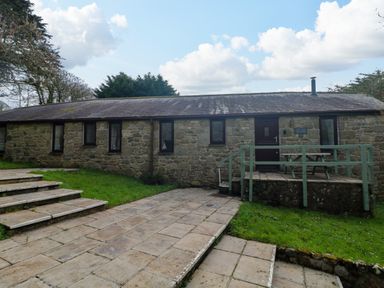 A stone building with several windows and a wooden door with steps and a small patio at The Old Piggeries in Gulval near Penzance