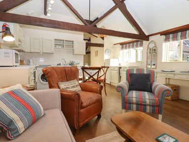 A living room and kitchen area with armchairs and wooden beams at The Calf Pen in Colyton