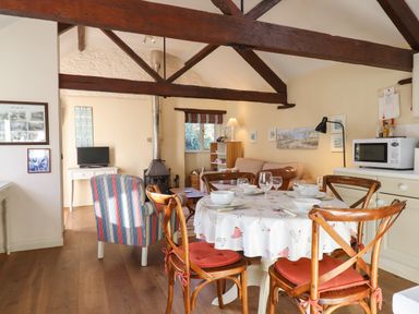 A dining area with a round table set for four and a living space with a sofa, armchair, wood stove, and TV at The Calf Pen in Colyton