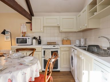 A kitchen with cream cabinets a stove a microwave and a dining table set with plates and glasses at The Calf Pen in Colyton