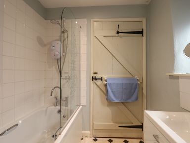 A bathroom with a bathtub shower and a door with a towel rack at The Calf Pen in Colyton