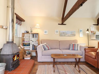 A living room with a wood stove fireplace a beige sofa a brown leather armchair wooden coffee table bookshelf and framed pictures on the wall at The Calf Pen in Colyton