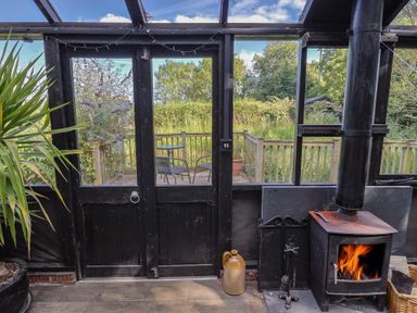 A conservatory with a stove and a view of the garden at The Calf Pen in Colyton